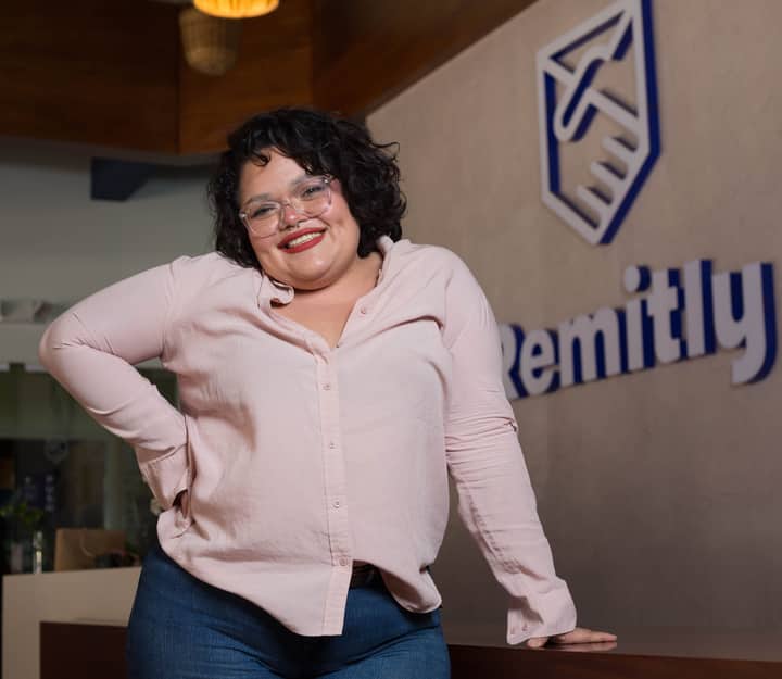 Plus-size woman smiling confidently with eyeglasses and pink shirt in an office.