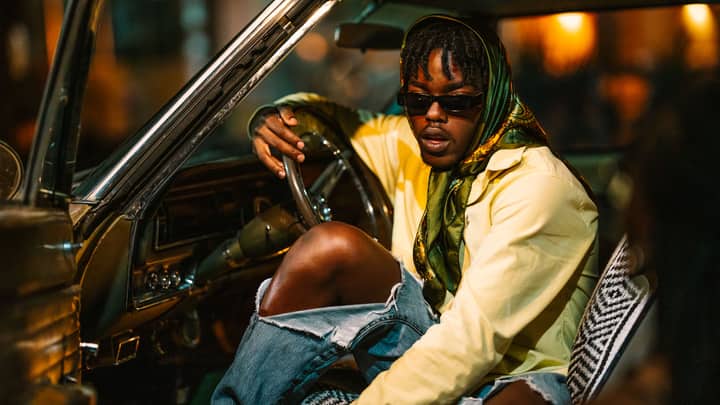 Trendy man wearing sunglasses sits in a vintage car with a yellow shirt and headscarf.