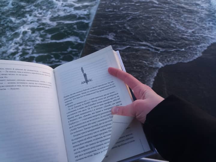 An open book in a person's hand near the ocean, signifying calm and knowledge.