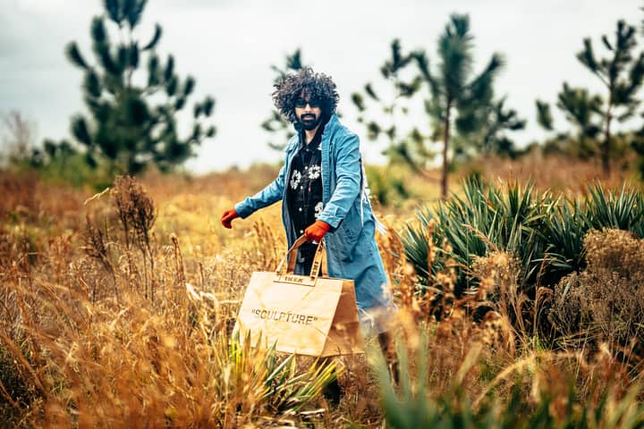 Stylish man in a blue coat walking through a picturesque field, carrying a designer bag.