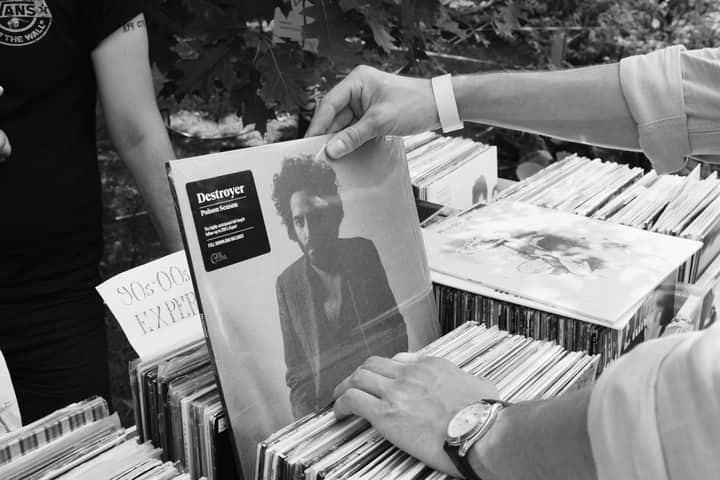 A close-up black and white shot of people browsing vinyl records at an outdoor market.