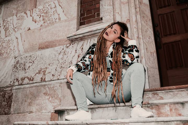 Fashionable woman with dreadlocks sitting on marble stairs in Bogotá, showcasing a modern urban look.