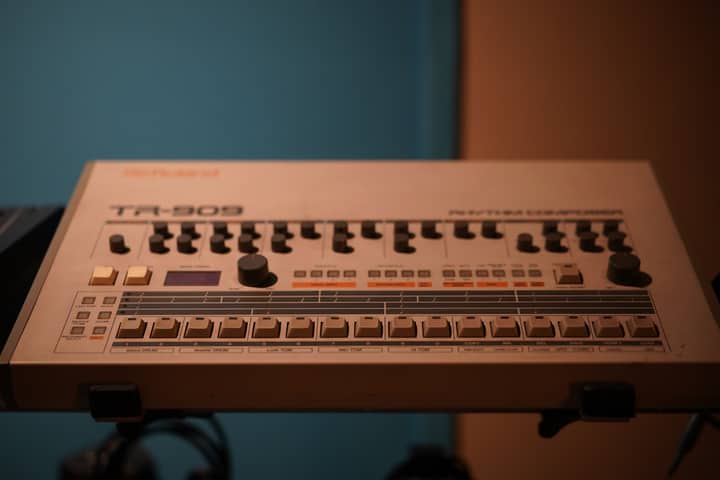 Close-up of a classic Roland TR-909 drum machine in a studio setting.