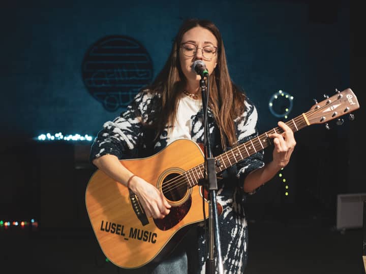 Woman performing music on stage with acoustic guitar and microphone.