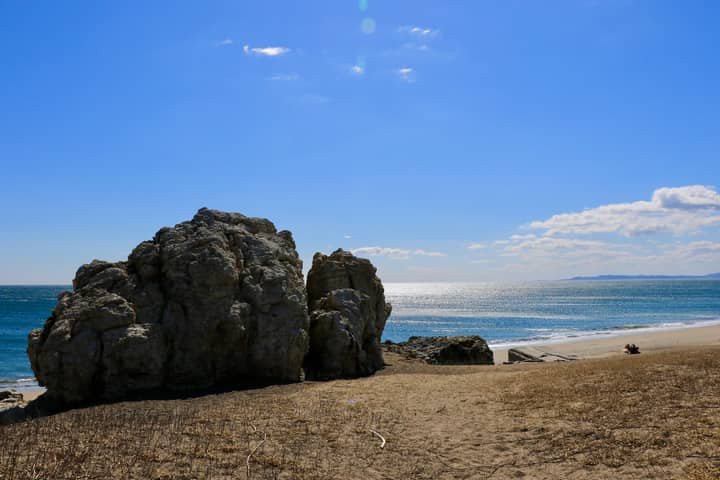 Peaceful beach scene featuring large rocks under a bright blue sky.