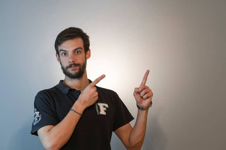 Man with beard and short hair wearing polo shirt pointing upward in studio.