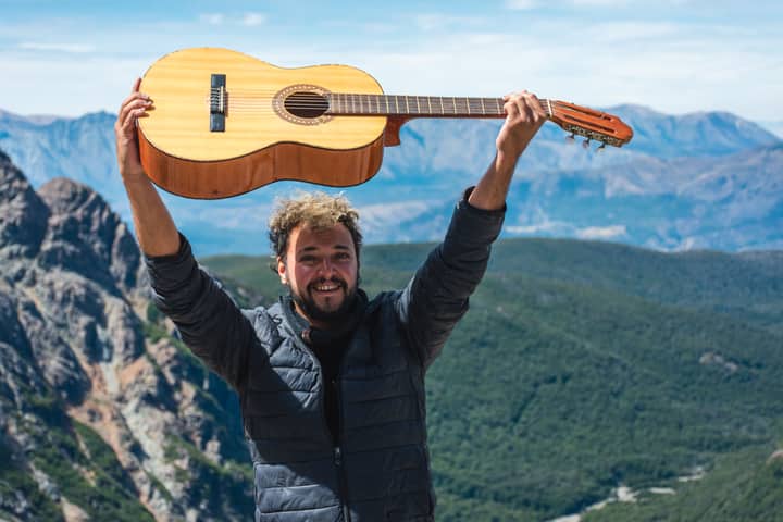 A joyful man lifts his guitar high in front of a majestic mountain landscape, celebrating music in nature.