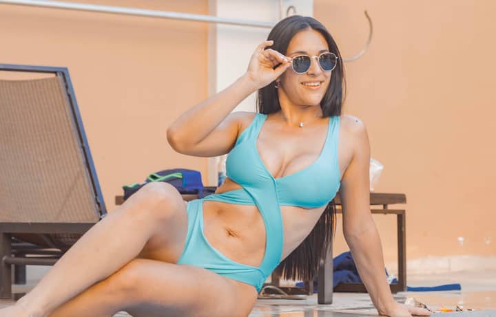 A woman in stylish blue swimwear enjoys a sunny day outdoors, wearing trendy sunglasses.