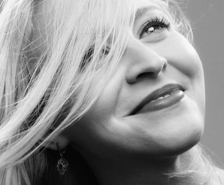 Close-up black and white portrait of a smiling woman with flowing hair, exuding elegance.