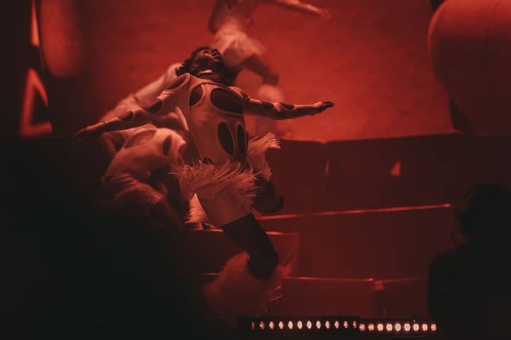 Energetic dancers performing on stage in striking red lighting and creative costumes.