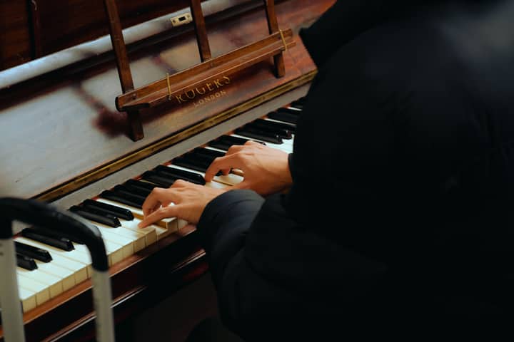Close-up of hands playing a Rogers London upright piano indoors.
