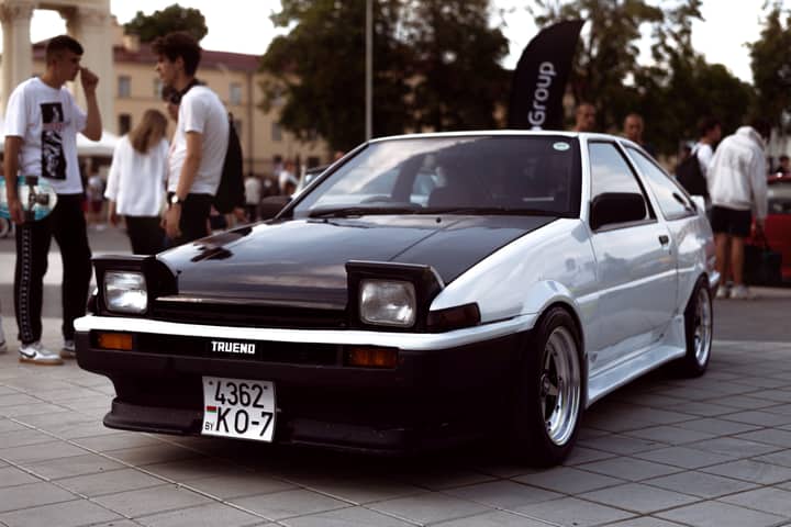 Toyota Sprinter Trueno displayed at outdoor car event with people in background.