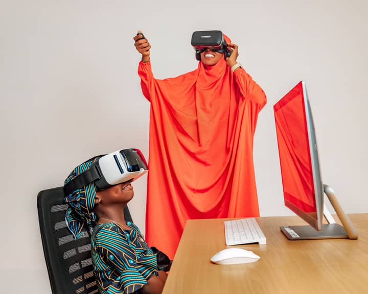 Two women enjoying VR technology indoors, combining traditional attire with modern virtual experiences.