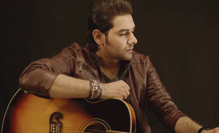 Portrait of a male musician with an acoustic guitar in a studio setting wearing a leather jacket.