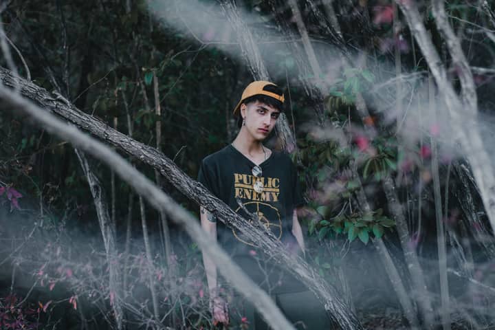 Man in black t-shirt and cap poses amid forest trees. Moody artistic portrait.