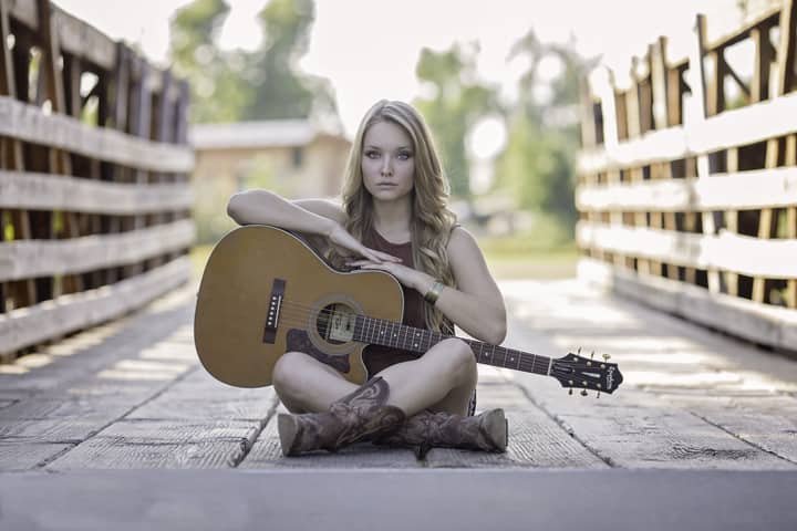 Artistic portrait of a young woman sitting with a guitar on a rustic wooden bridge.