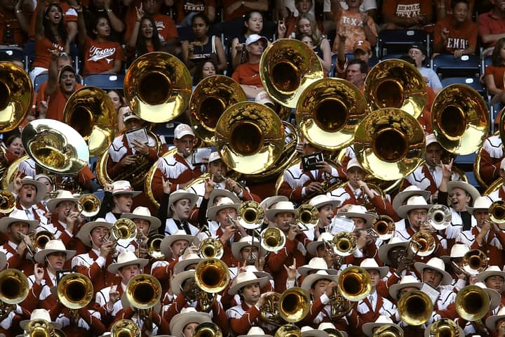 A lively marching band performs with brass instruments at a crowded sports stadium.