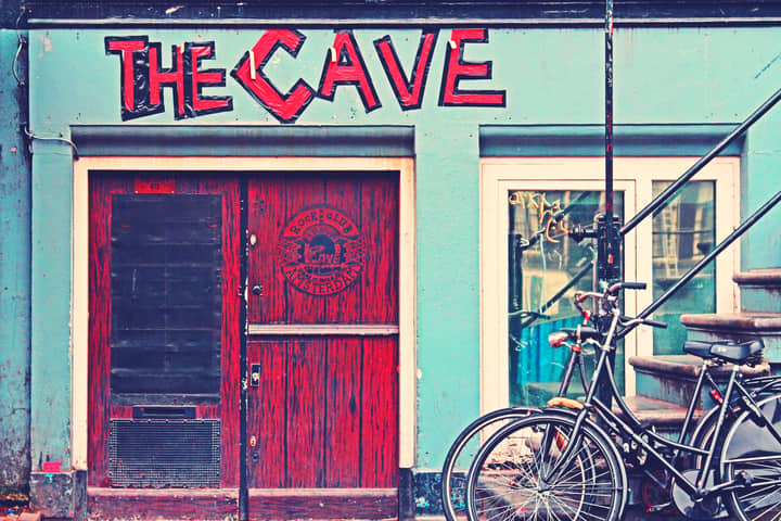 Vibrant facade of The Cave rock club in Amsterdam, featuring bicycles and outdoor stairs.