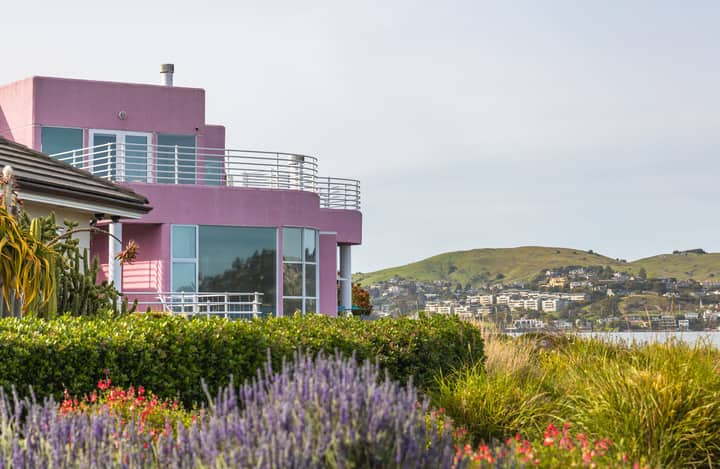A modern pink house with a balcony offers breathtaking sea views amid lush greenery and hills in summer.