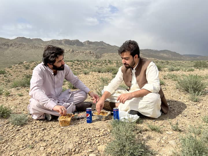 Two men sharing a meal outdoors in Quetta, Balochistan with scenic mountain views.