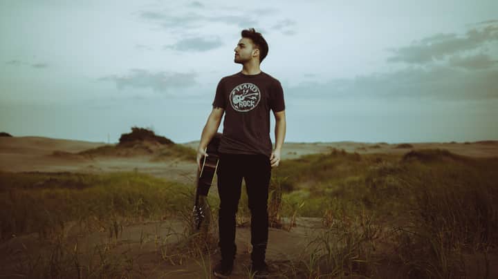 Casual portrait of a young musician standing on beach dunes with a guitar, capturing a relaxed vibe.