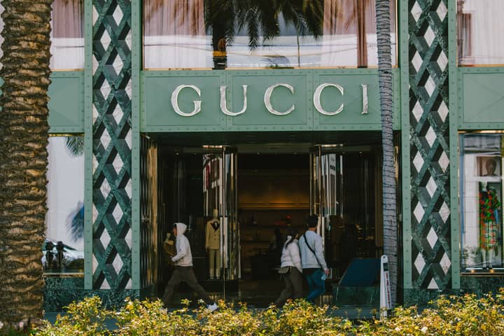 Gucci store facade with people passing by on a sunny day.