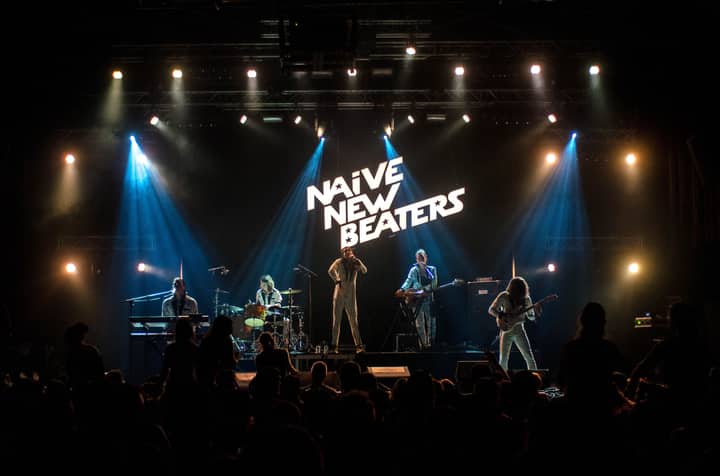 A vibrant live performance by a band on stage with dramatic lighting and engaging crowd.