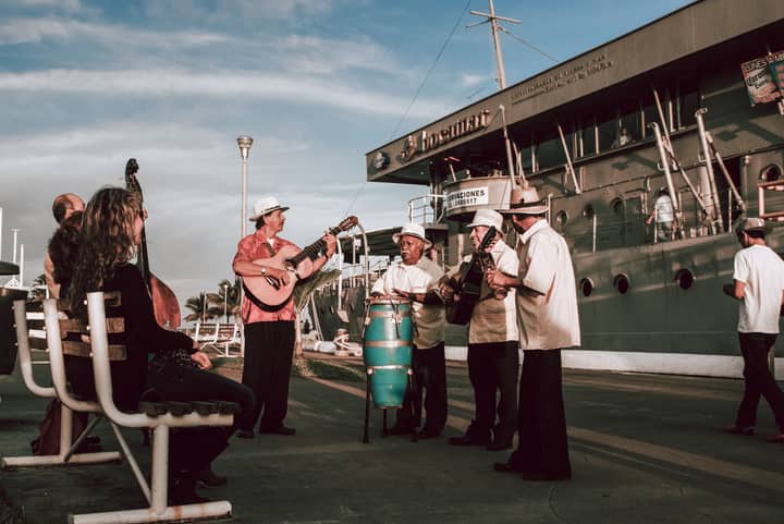 A group of musicians performing outdoors near a ship in Veracruz harbor, creating a lively urban scene.