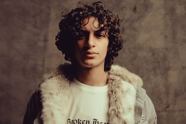 Stylish portrait of a young man with curly hair wearing a fur jacket in a studio setting.