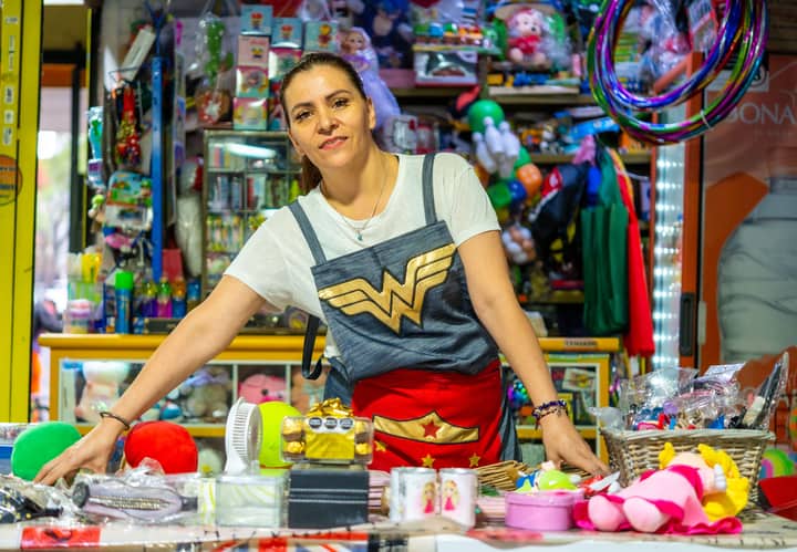 A smiling woman sells colorful toys and souvenirs at a vibrant market in Ciudad de México.