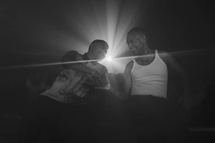 Two men in a dim setting share a laugh with dramatic lighting creating a striking visual effect.