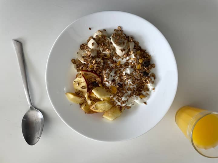 A nutritious breakfast meal featuring granola, banana, and apples served with orange juice.