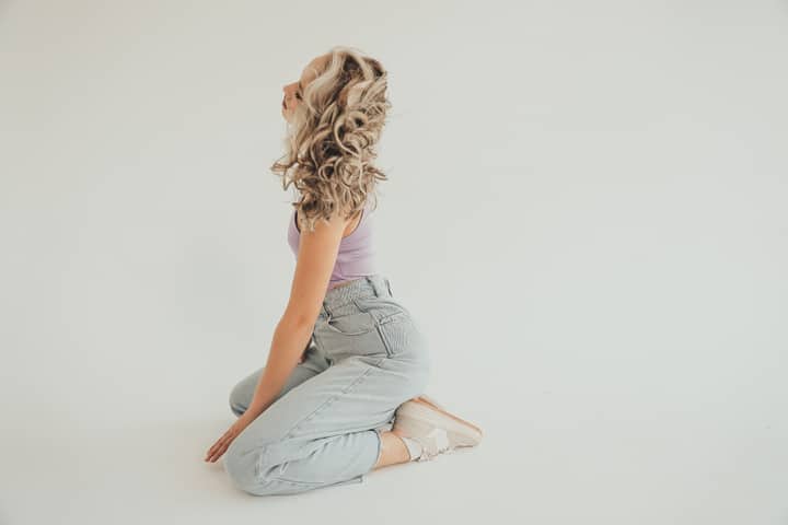 A fashionable woman with curly hair poses in denim jeans against a white background, exuding style and grace.