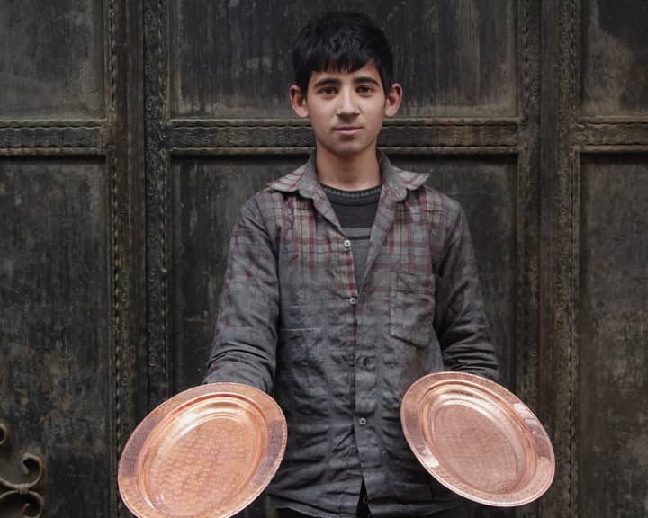 A young artisan proudly displaying handcrafted copper plates, showcasing traditional craftsmanship.