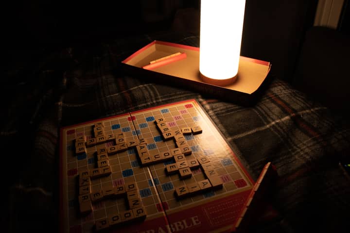Dimly lit room with a Scrabble board game and a warm lamp creating an intimate setting.