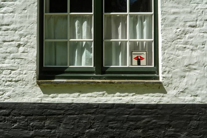 Close-up of a traditional window in Brugge with a unique 'Shhh' sign.