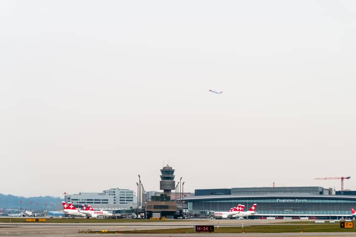 Swiss airplanes at Zurich Airport with control tower and terminal in background.