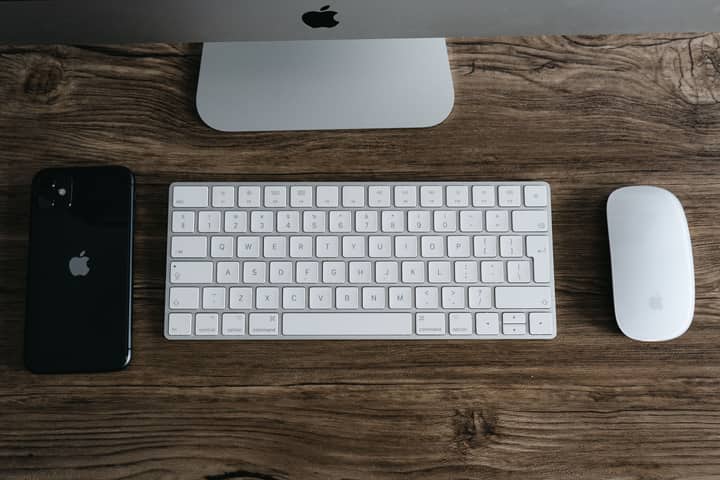 A minimalist workspace featuring a smartphone, keyboard, and mouse on a wooden desk.