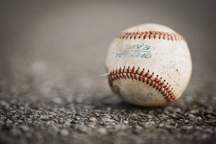 Detailed close-up of a worn baseball resting on a textured asphalt ground, emphasizing its use in sports.