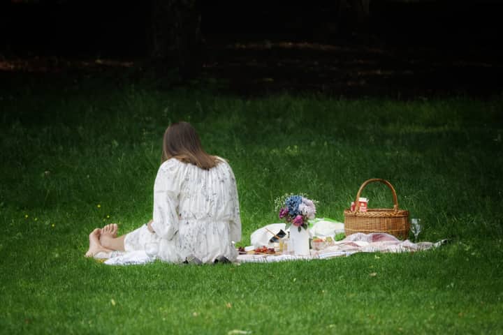 A woman enjoys a peaceful picnic in Oslo, surrounded by nature, flowers, and a basket.