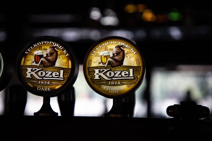 Close-up of Kozel beer tap handles showcasing premium lager and dark beer branding in a cozy bar setting.