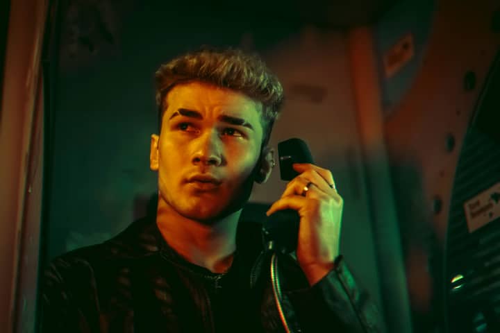Portrait of a young man in a telephone booth holding a phone with dramatic lighting.