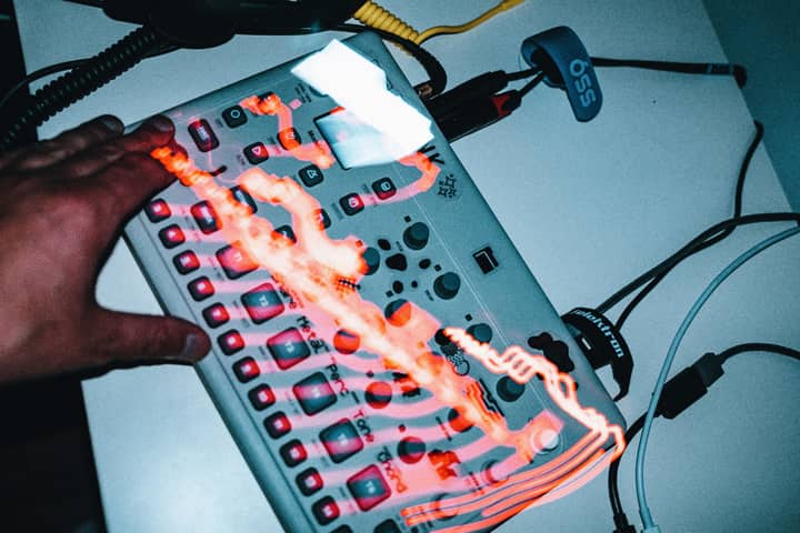 A close-up of a hand on an electronic music device with glowing lights and cables. Perfect for music and technology themes.