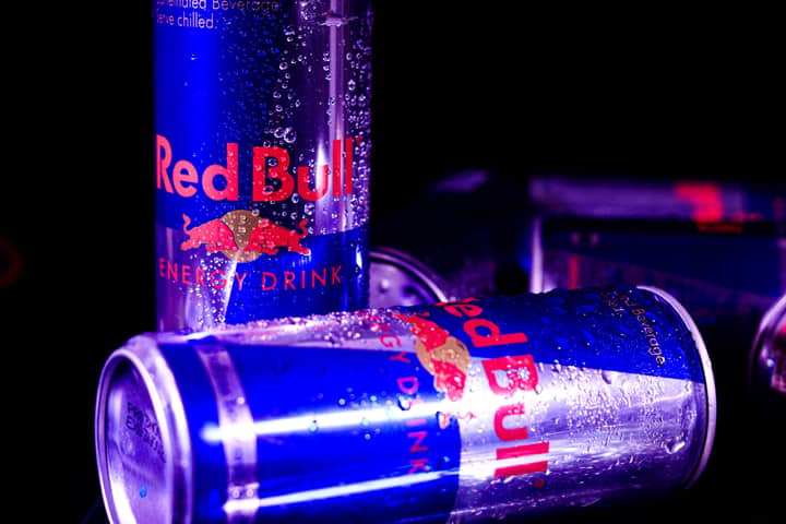 Close-up of chilled Red Bull cans with water droplets, reflecting vibrant neon lighting.