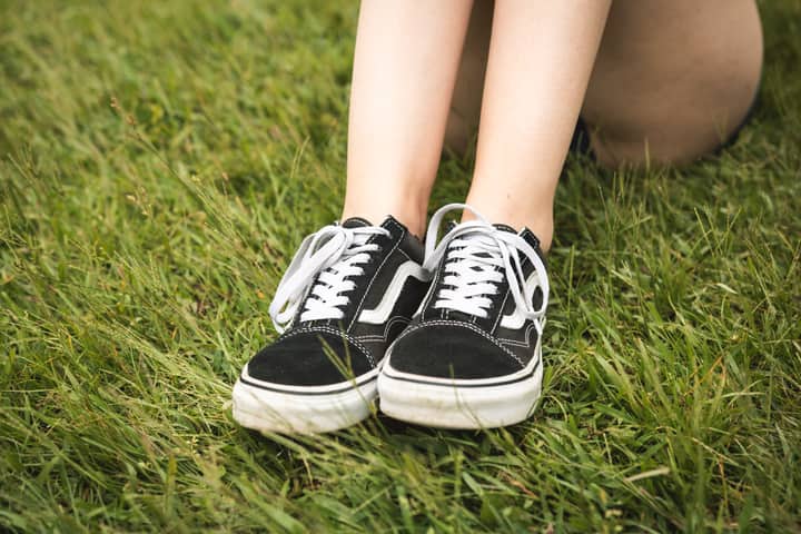 Woman relaxing outdoors, showcasing black Vans sneakers on a grassy field.