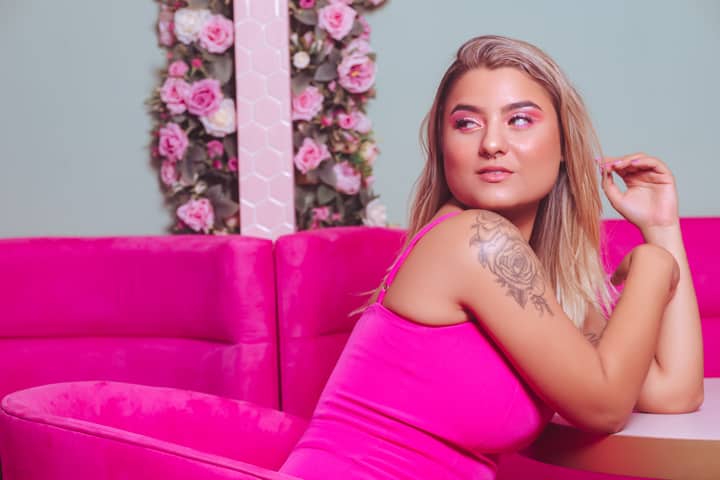 Elegant woman poses on a pink sofa in a floral setting, exuding style and confidence.