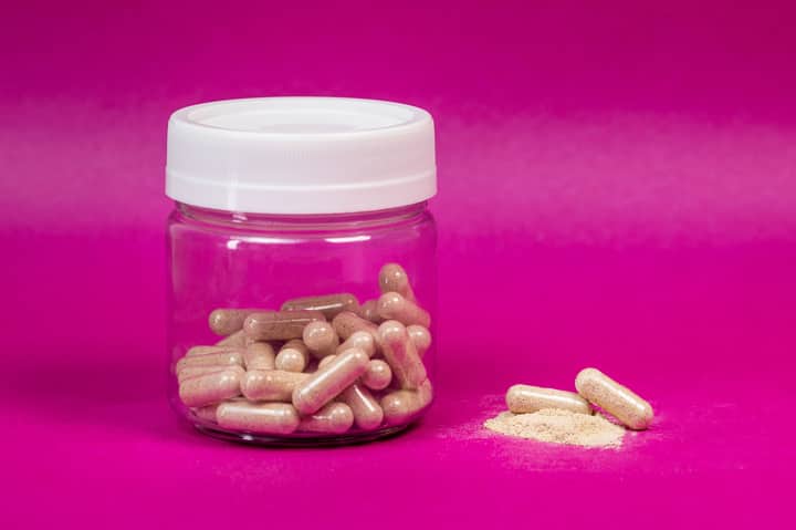 A glass jar filled with capsules on a vibrant pink background, showcasing health supplements.