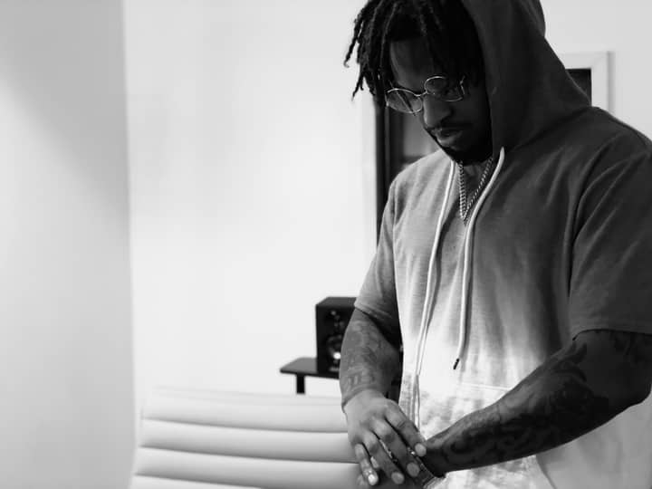 A man in a hoodie looks thoughtful indoors, captured in black and white.