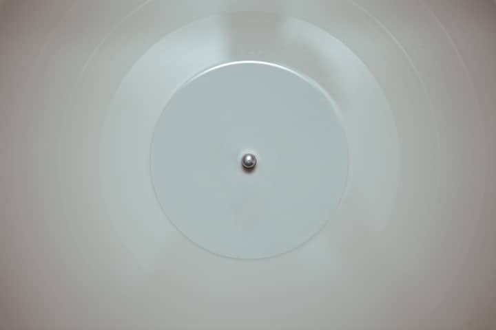 A close-up of a white vinyl record spinning on a turntable, highlighting its minimalist design.
