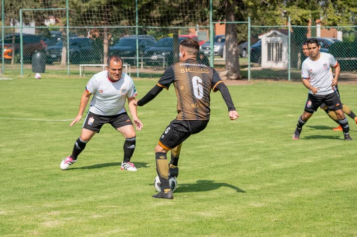 Adult men playing a friendly soccer game on a grassy field under clear skies.